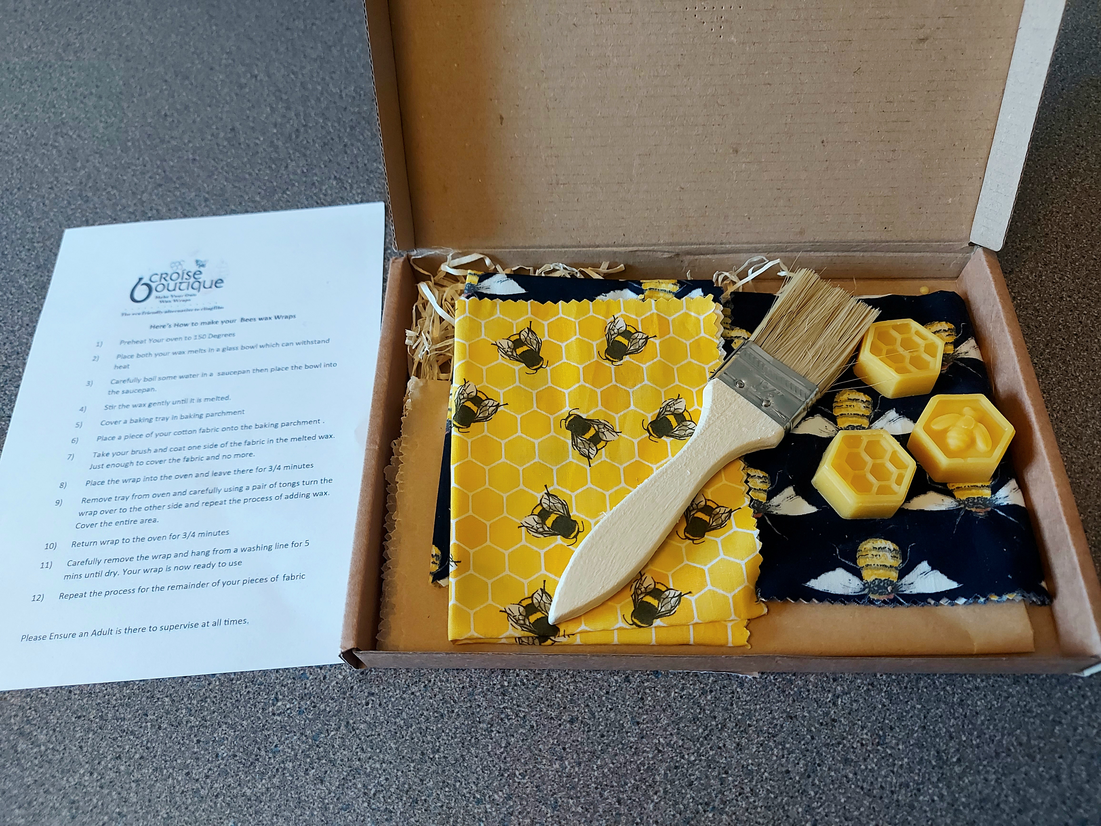 a cardboard box containing a beeswax wrap kit; fabric, beeswax, a brush and baking paper