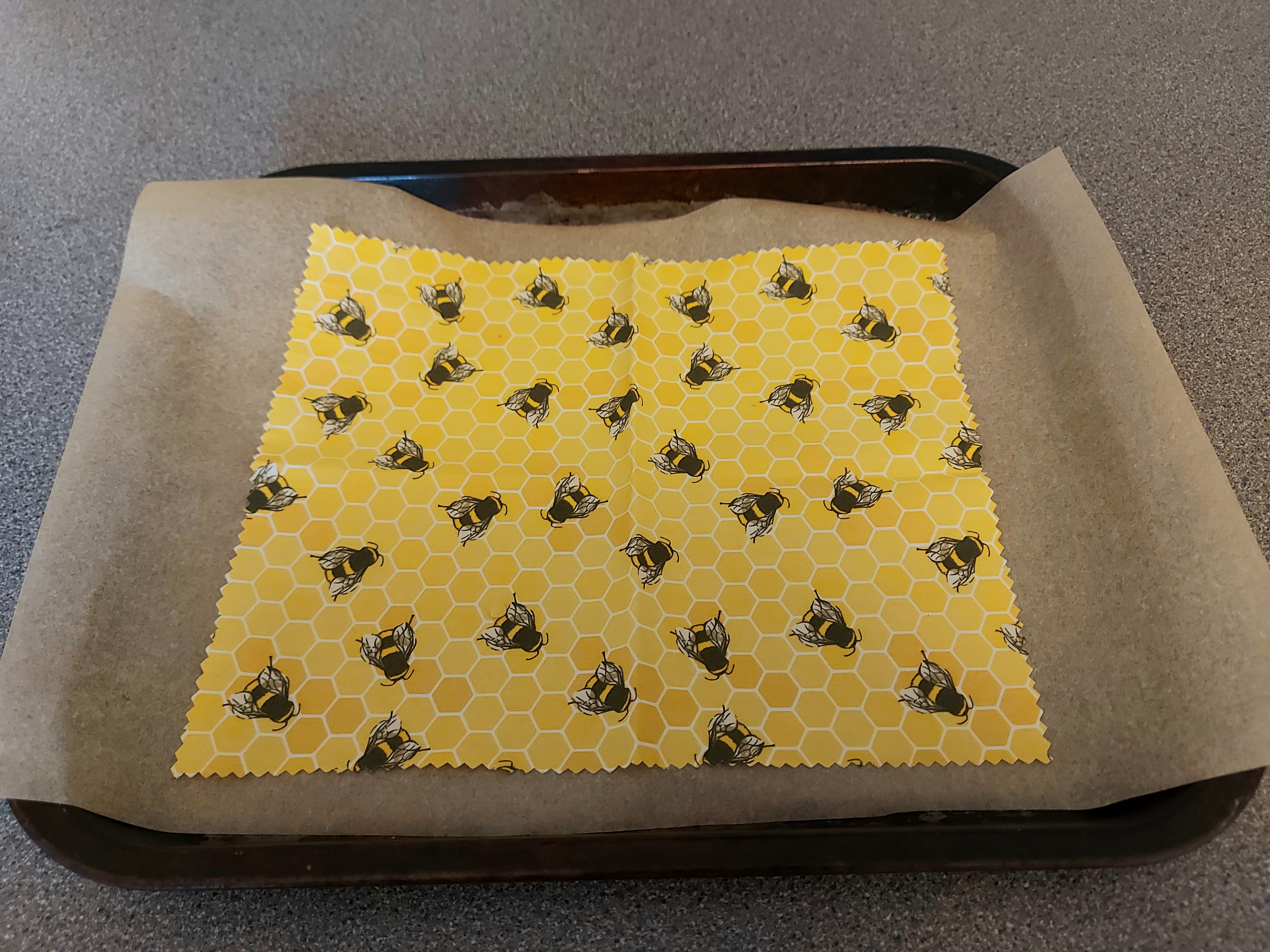 a yellow piece of fabric patterned with bees on a baking tray
