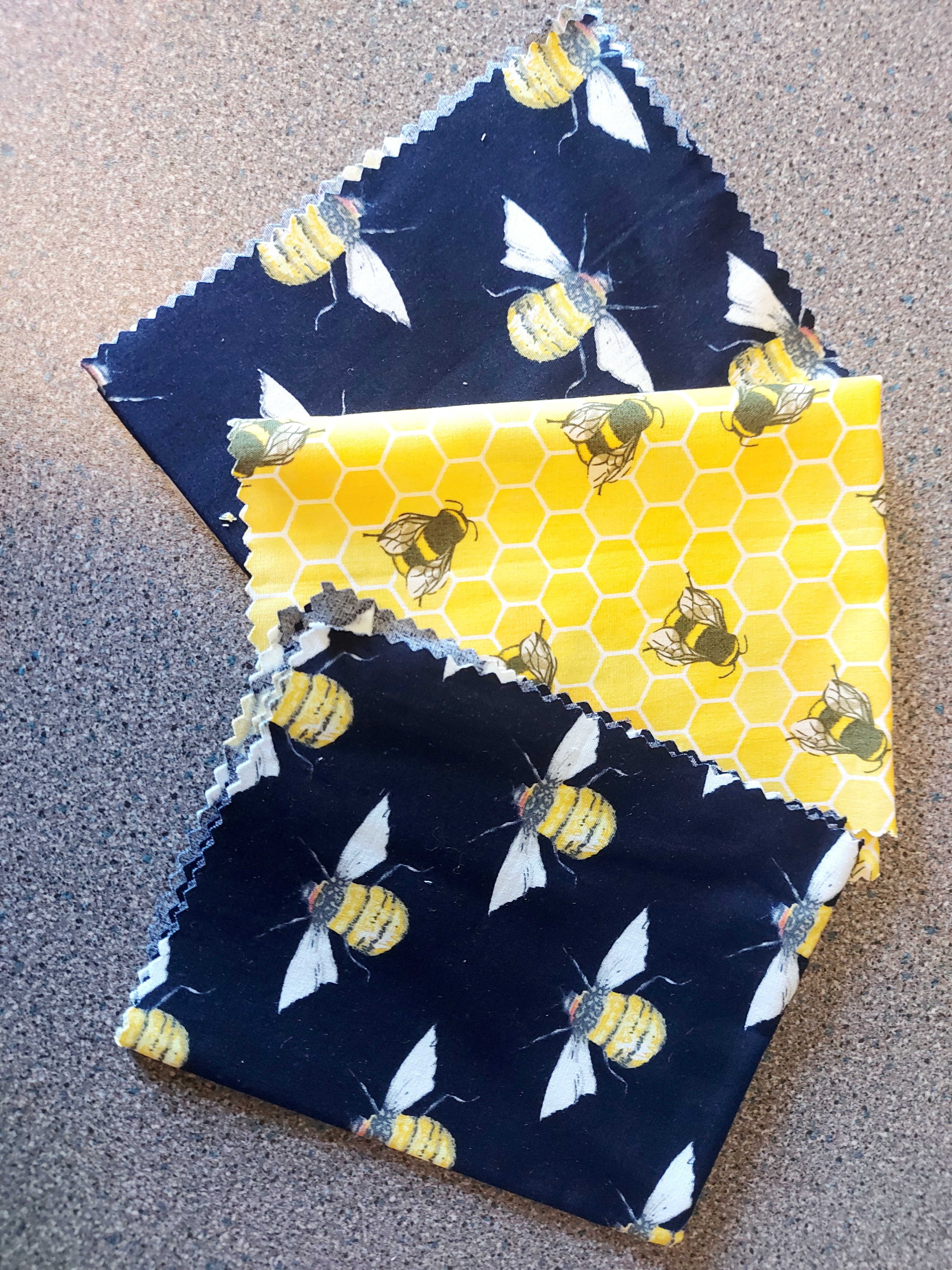 three piees of patterned fabric; two show bumblebees on dark blue fabric, one shows bumblebees on yellow fabric