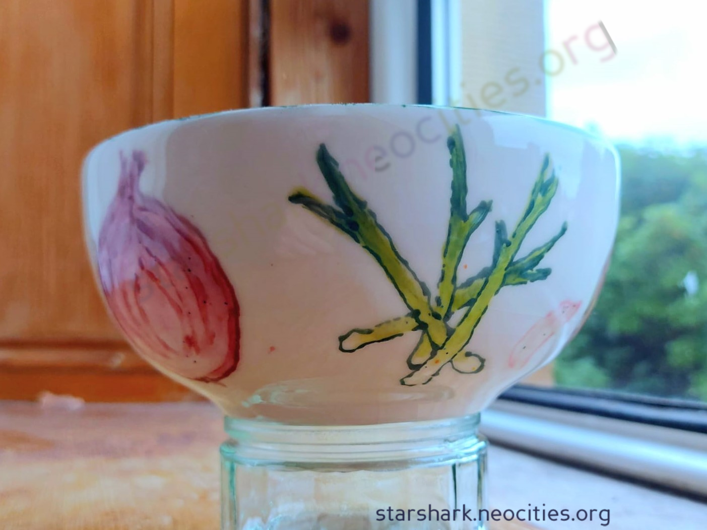 a ceramic cereal bowl painted with varius alliums: spring onions and a red onion are visible.