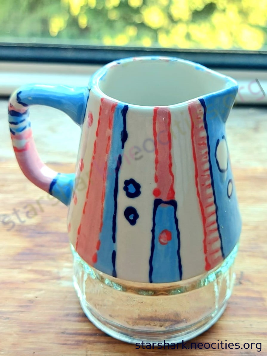 a ceramic milk jug painted in blue, pink and white.