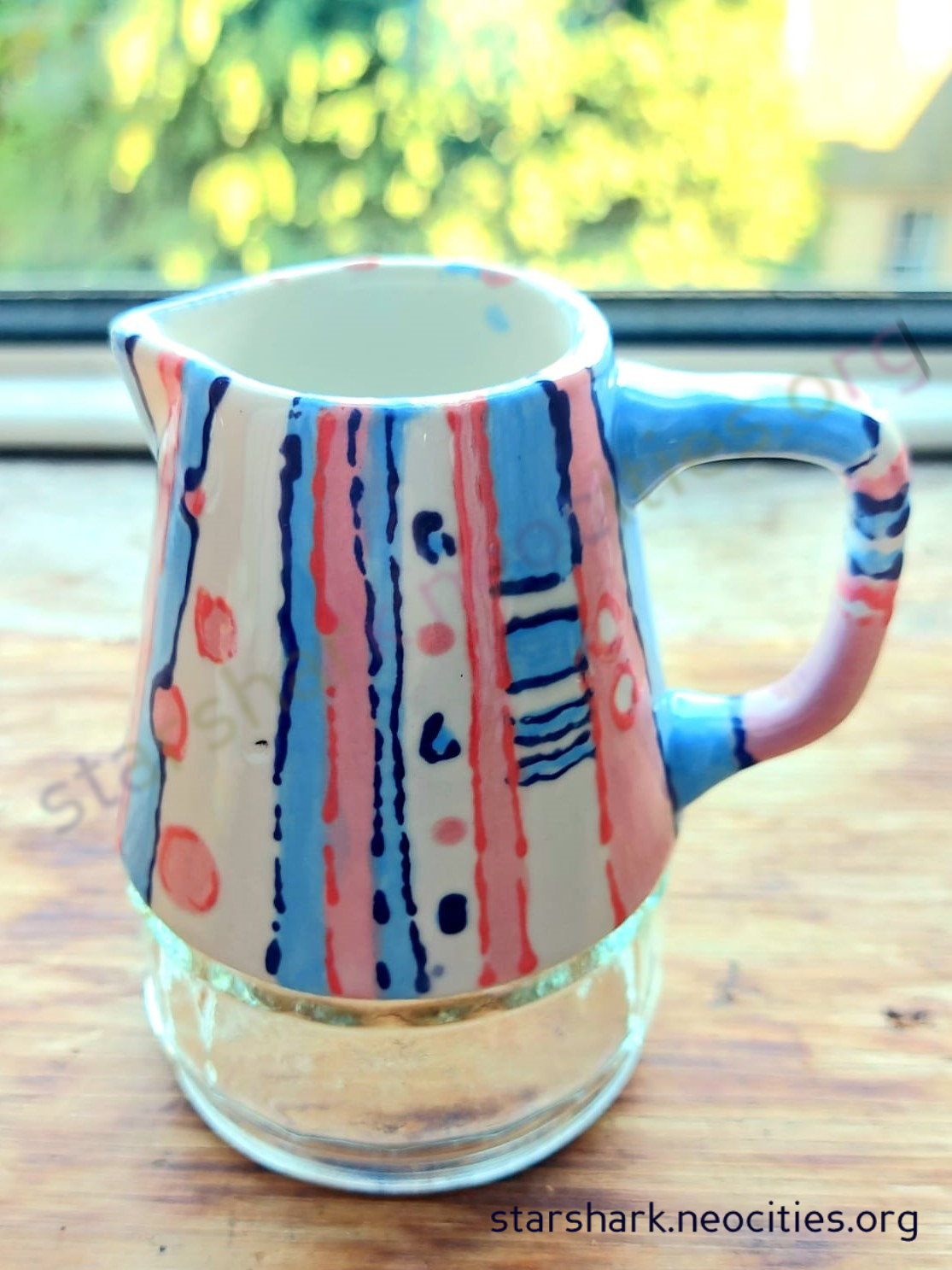 a ceramic milk jug painted in blue, pink and white.